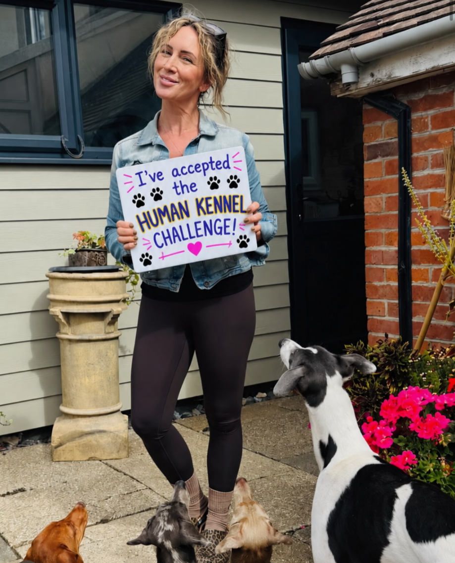 Clare Westwood holding her "I've accepted the Human Kennel Challenge" board, surrounded by her dogs